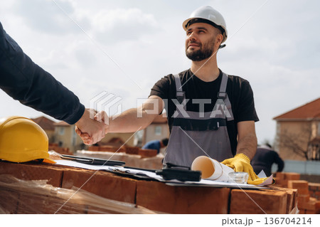 Handshake, making a deal. Cooperation between construction site worker and businessman Handshake, making a deal. Cooperation between construction site worker and businessman 136704214