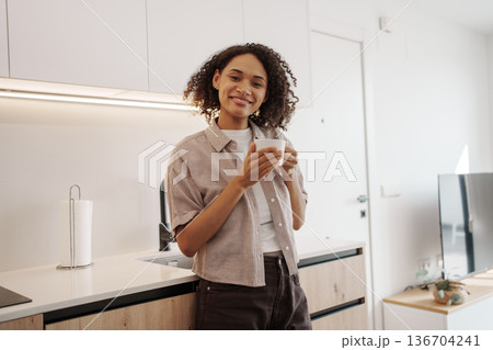 Relaxed Woman Standing Confidently In Modern Kitchen Sipping Coffee During Routine Morning 136704241