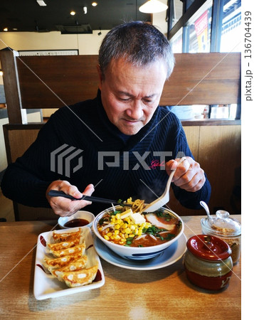 ラーメン屋でラーメンギョーザを食べる元気な中年男性 136704439