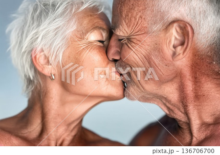 Elderly couple kisses in a close-up side profile, highlighting sunlit skin, natural wrinkles, and short white hair with a soft background 136706700