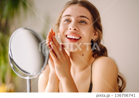 Young woman with problem skin looking into mirror. Concept of acne therapy, scars Young woman with problem skin looking into mirror. Concept of acne therapy, scars 136706741