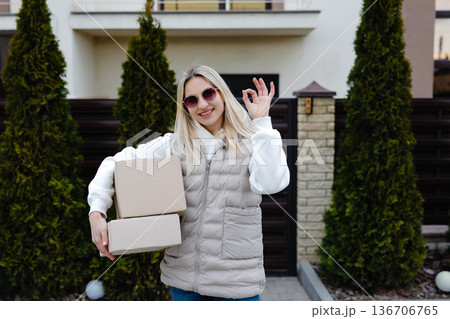 Delivery woman holding cardboard boxes and gesturing ok sign Delivery woman holding cardboard boxes and gesturing ok sign 136706765