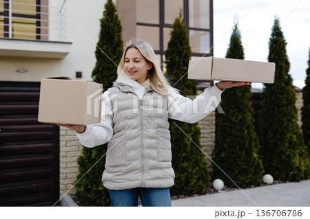 Delivery woman holding two cardboard boxes in front of a house 136706786