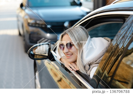 Happy blonde woman enjoying road trip leaning out of car window Happy blonde woman enjoying road trip leaning out of car window 136706788
