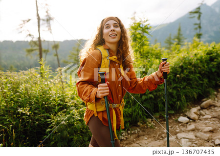 Young woman traveler hiking poles on trail among the mountains. Hiking. Active lifestyle. 136707435
