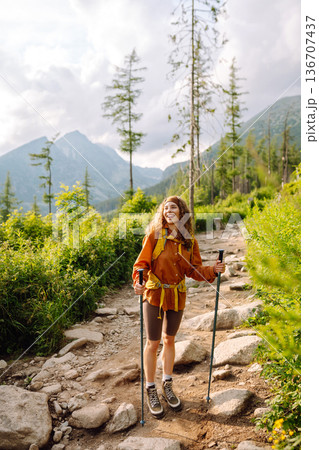 Young woman traveler hiking poles on trail among the mountains. Hiking. Active lifestyle. 136707437