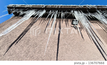 Icicles of ice hang from a roof gutter and a floodlight Icicles of ice hang from a roof gutter and a floodlight 136707668