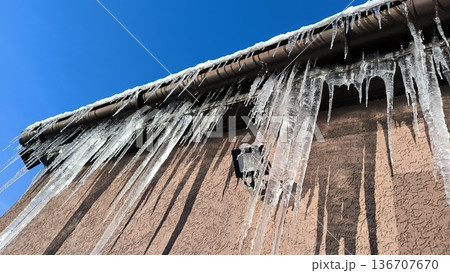 Icicles of ice hang from the roof drainpipe of a house and a floodlight Icicles of ice hang from the roof drainpipe of a house and a floodlight 136707670