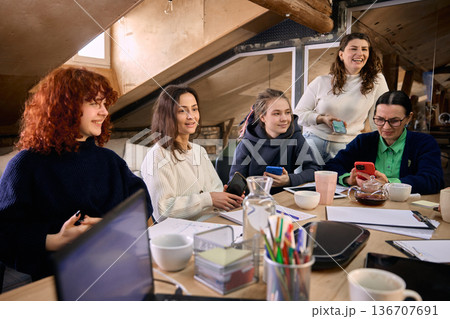 Female team gathered around table reviewing online campaign results. Female team gathered around table reviewing online campaign results. 136707691