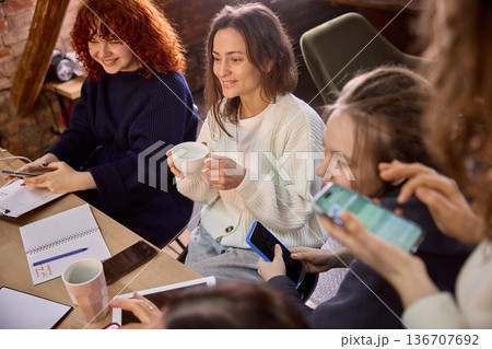 Women colleagues checking mobile analytics during strategy session. 136707692