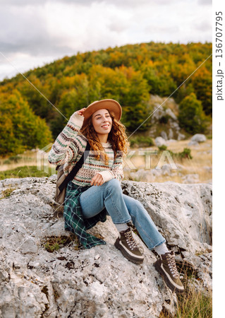 Young woman enjoys sunny afternoon in mountains while sitting on rocks. Tourism. Active lifestyle. Young woman enjoys sunny afternoon in mountains while sitting on rocks. Tourism. Active lifestyle. 136707795