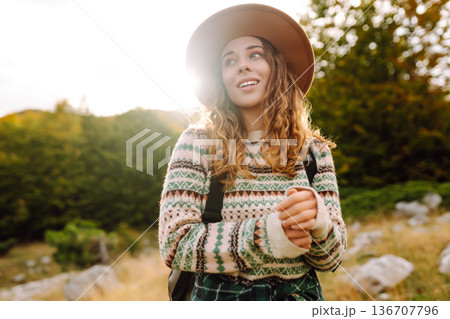 Young woman enjoys sunny afternoon in mountains while sitting on rocks. Tourism. Active lifestyle. 136707796