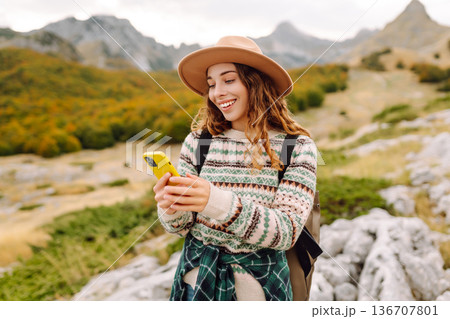 Woman is seen smiling, holding yellow phone in autumn landscape. Enjoying fresh air after hiking. Woman is seen smiling, holding yellow phone in autumn landscape. Enjoying fresh air after hiking. 136707801