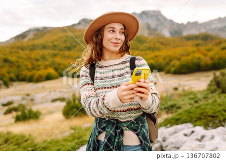 Woman is seen smiling, holding yellow phone in autumn landscape. Enjoying fresh air after hiking. Woman is seen smiling, holding yellow phone in autumn landscape. Enjoying fresh air after hiking. 136707802