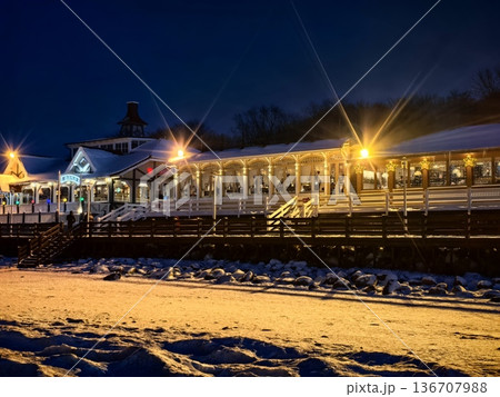 View of a coastal illuminated cafe from the frozen shore in winter at sunset View of a coastal illuminated cafe from the frozen shore in winter at sunset 136707988