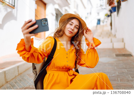 Young woman to take a quick selfie as a souvenir of her trip in a sunny village. Tourist Adventure 136708040