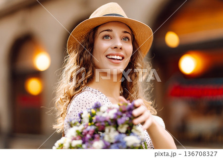 Happy young woman with a bouquet of wild flowers walks on the street city. Emotions. Fashion style Happy young woman with a bouquet of wild flowers walks on the street city. Emotions. Fashion style 136708327