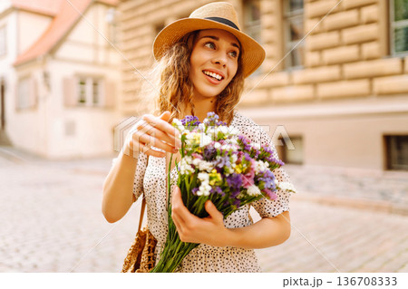 Happy young woman with a bouquet of wild flowers walks on the street city. Emotions. Fashion style Happy young woman with a bouquet of wild flowers walks on the street city. Emotions. Fashion style 136708333