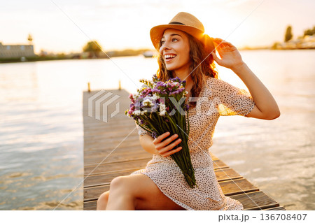 Young woman in dress sitting on wooden pier near pond. Rustic style of wedding. Travel, tourism Young woman in dress sitting on wooden pier near pond. Rustic style of wedding. Travel, tourism 136708407