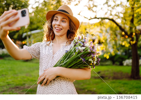 Young woman with blossoming flower bouquet taking selfie on cellphone outdoor. Blogging concept. Young woman with blossoming flower bouquet taking selfie on cellphone outdoor. Blogging concept. 136708415