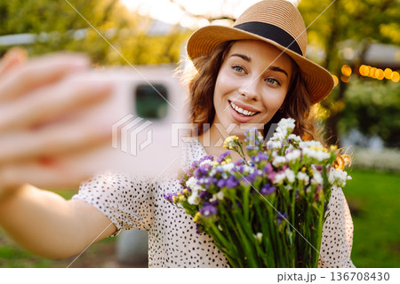 Young woman with blossoming flower bouquet taking selfie on cellphone outdoor. Blogging concept. 136708430