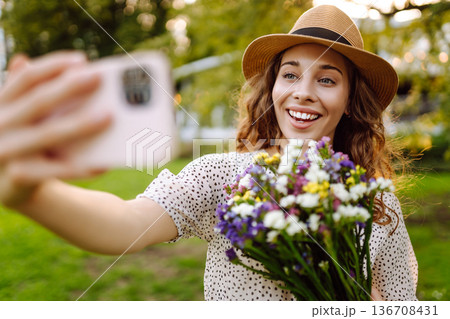 Young woman with blossoming flower bouquet taking selfie on cellphone outdoor. Blogging concept. 136708431