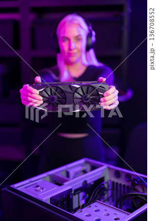 Female gamer in her 20s upgrades a gaming PC with high-end graphics card in neon-lit setup Female gamer in her 20s upgrades a gaming PC with high-end graphics card in neon-lit setup 136708552