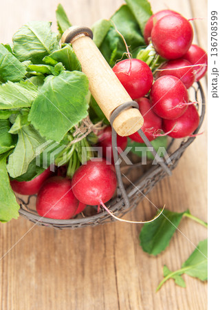 Fresh red radishes with green leaves in basket on wood Fresh red radishes with green leaves in basket on wood 136708599
