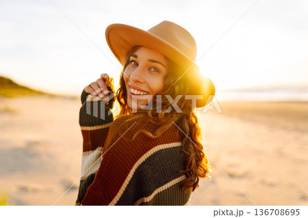 Beautiful curly woman on beach in cold sunny weather, deeply breathing fresh ocean breeze. Lifestyle 136708695