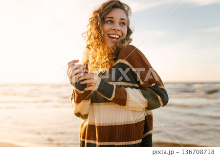 Portrait of a beautiful woman on the beach at sunset. Girl walks along the beach and enjoys weather 136708718