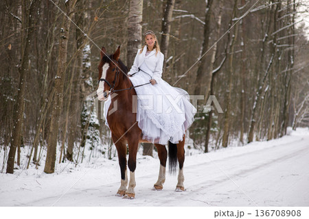 Bride Smiling While Riding Horse Through Winter Woods 136708908