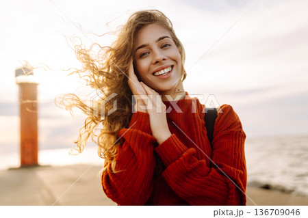 Young woman enjoying a breezy day near a vibrant red lighthouse. Autumn sunset Young woman enjoying a breezy day near a vibrant red lighthouse. Autumn sunset 136709046