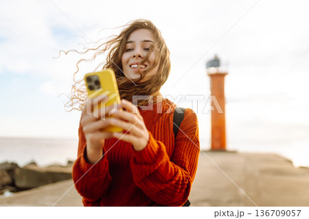 Young woman smiling and using her smartphone at the beach sunset. Blogging, communication concept. Young woman smiling and using her smartphone at the beach sunset. Blogging, communication concept. 136709057