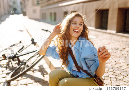 Beautiful smiling woman sitting next to bike on the street city. Adventure Concept 136709137