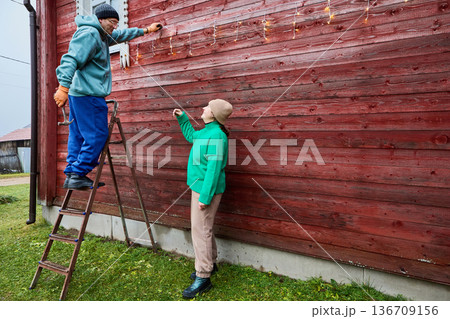 Villagers adorn house for Christmas hanging garland along walls. Villagers adorn house for Christmas hanging garland along walls. 136709156