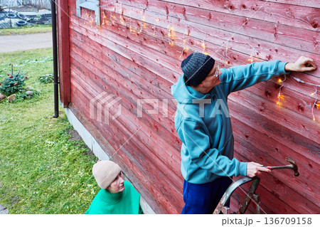 On Christmas eve married couple decorates facade of country house. On Christmas eve married couple decorates facade of country house. 136709158