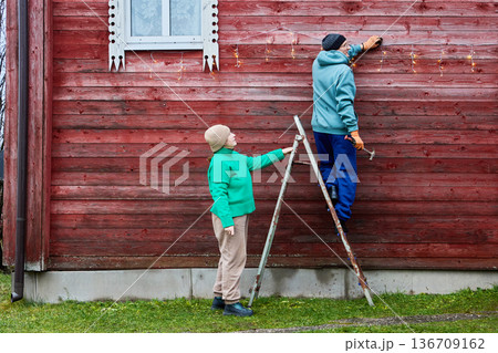 Installing string lights on facade of wooden farm building. Installing string lights on facade of wooden farm building. 136709162