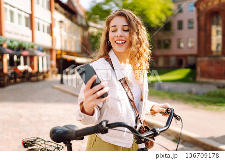 Woman using mobile phone, walks with bicycle, looks around at beautiful architecture. Selfie time. 136709178