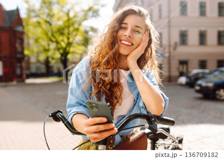 Woman using mobile phone, walks with bicycle, looks around at beautiful architecture. Selfie time. 136709182