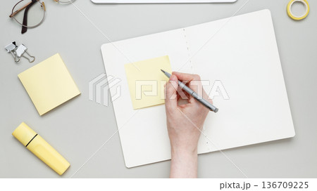 Woman writing on sticky note at organized workspace with notebook and stationery items Woman writing on sticky note at organized workspace with notebook and stationery items 136709225