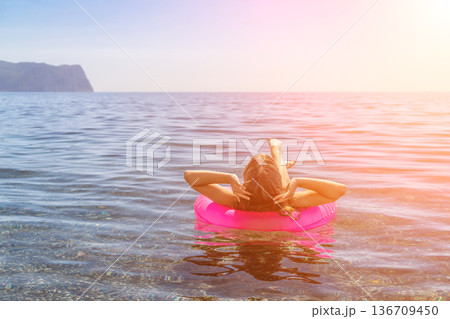 Woman sea inflatable floating on a pink ring in calm ocean water during a sunny summer vacation at the beach Woman sea inflatable floating on a pink ring in calm ocean water during a sunny summer vacation at the beach 136709450