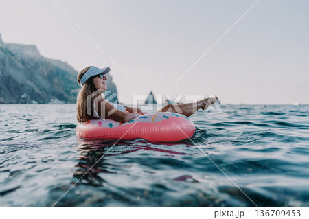 Woman, float, ocean. Young woman relaxing on a donut inflatable in the sea with scenic cliffs. 136709453