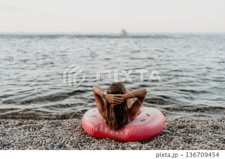 Woman, beach, relaxing. Young woman relaxing on a donut float at a pebble beach enjoying summer vacation. 136709454