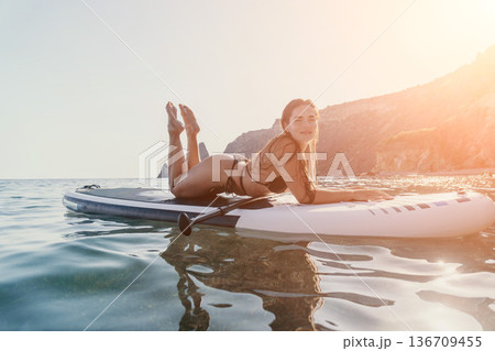 Woman Paddleboard Beach Relaxing on a paddleboard in the ocean near a beach. Woman Paddleboard Beach Relaxing on a paddleboard in the ocean near a beach. 136709455