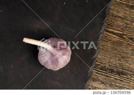 ripe purple garlic is scattered on a black table in the kitchen, garlic spices are on a black slate board in the over cooking 136709596
