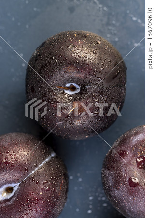 black fresh juicy wet plums on the kitchen table, several clean black plums on the table, the plums are covered with a lot of drops of water 136709610