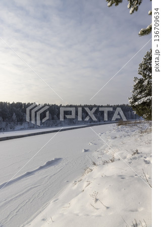 a wide river that is almost frozen in winter after frosts, a small river that is not frozen after severe frosts, the rest of the river is covered with ice and fresh snow 136709634