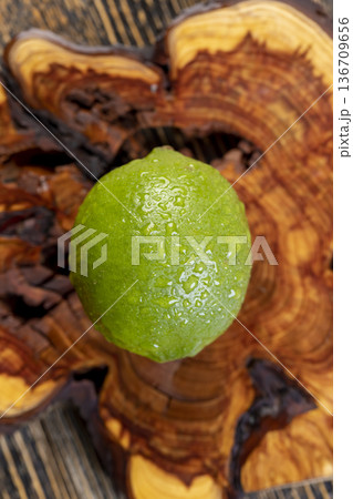 wet ripe citrus limes scattered on the wooden table in the kitchen, ripe and juicy lime for cooking, green limes covered with drops of water 136709656