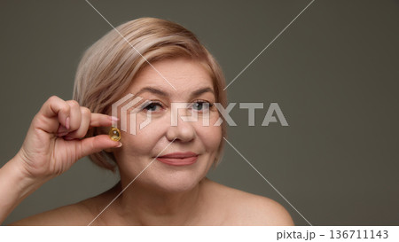 Older woman holding vitamin capsule for hair care. 136711143