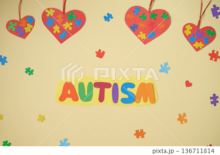 The inscription autism on a yellow background decorated with multicolored puzzle pieces and hearts suspended on a ribbon. Autism Awareness The inscription autism on a yellow background decorated with multicolored puzzle pieces and hearts suspended on a ribbon. Autism Awareness 136711814